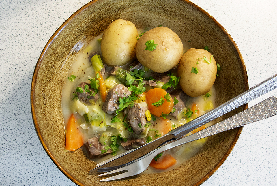 Kalvefrikassé med gulerødder, porre og selleri i lys sauce, serveret med kogte kartofler og persille.